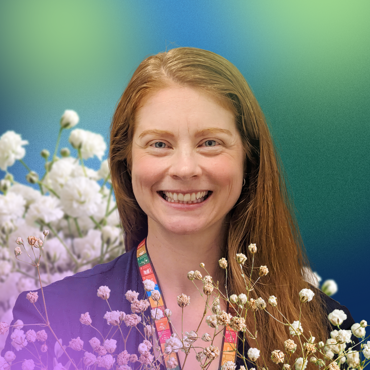Kelly Stumbaugh smiling, wearing a purple top and colorful lanyard, with a blue-green gradient background and white and pink wildflowers in the foreground